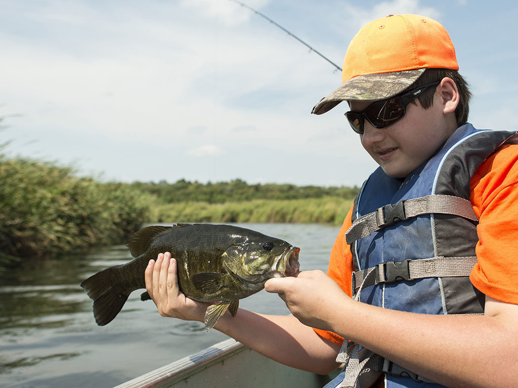 Best Summer Bass Lures Kid Holding a Largemouth Bass on a Boat.
